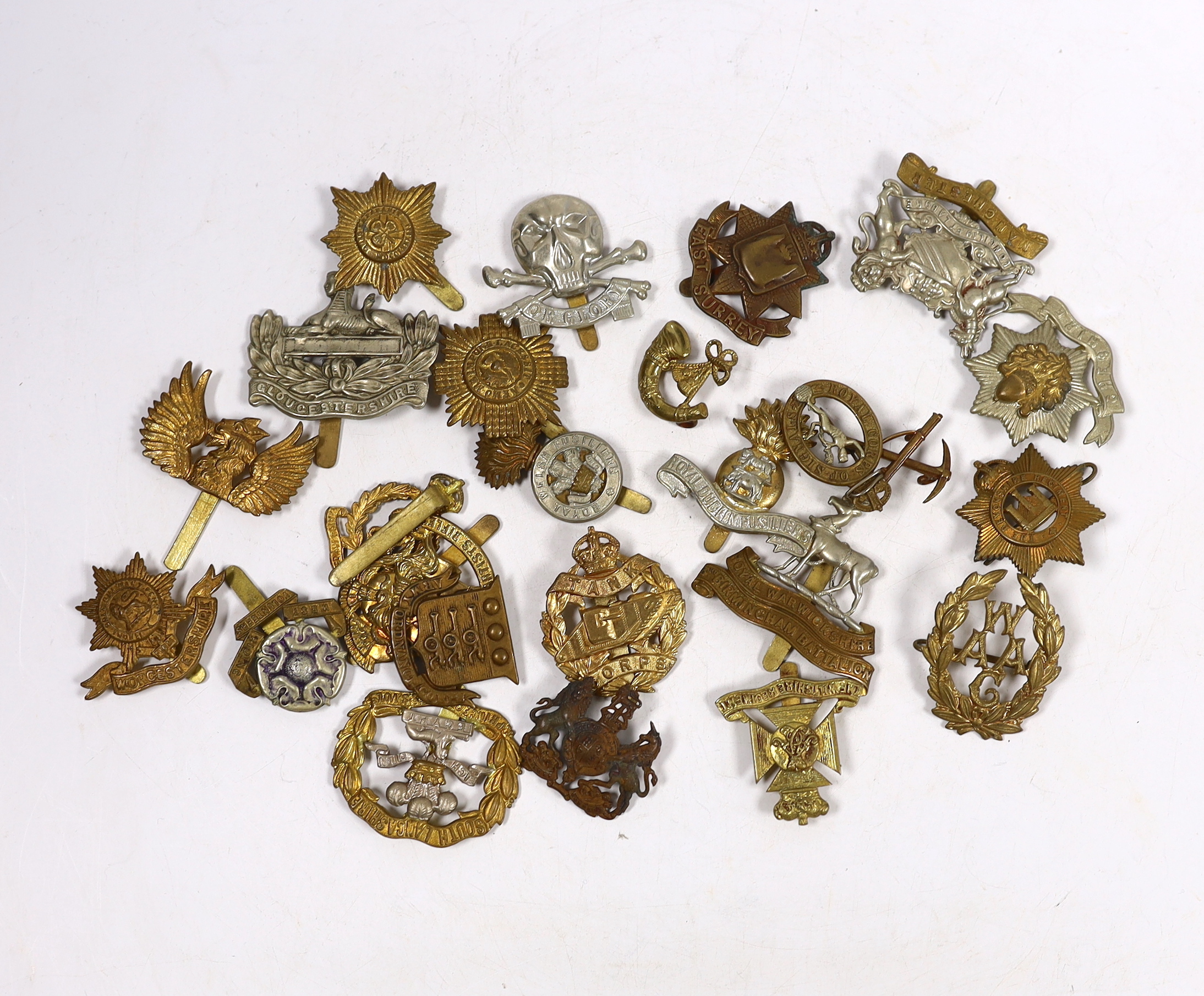 Twenty-five military cap badges including Gloucestershire Regiment, East Surrey, West Riding Volunteers, Wiltshire Regiment, Army Ordinance Corps, Worcestershire, Royal Warwickshire, Royal Dublin Fusiliers, RAMC, Royal W